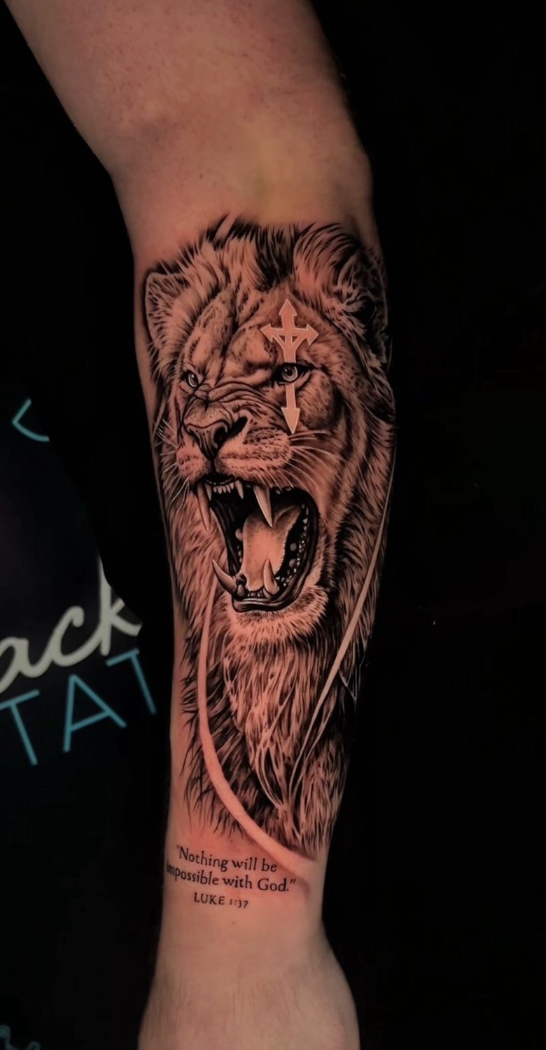 Black and grey roaring lion with cross and scripture forearm tattoo